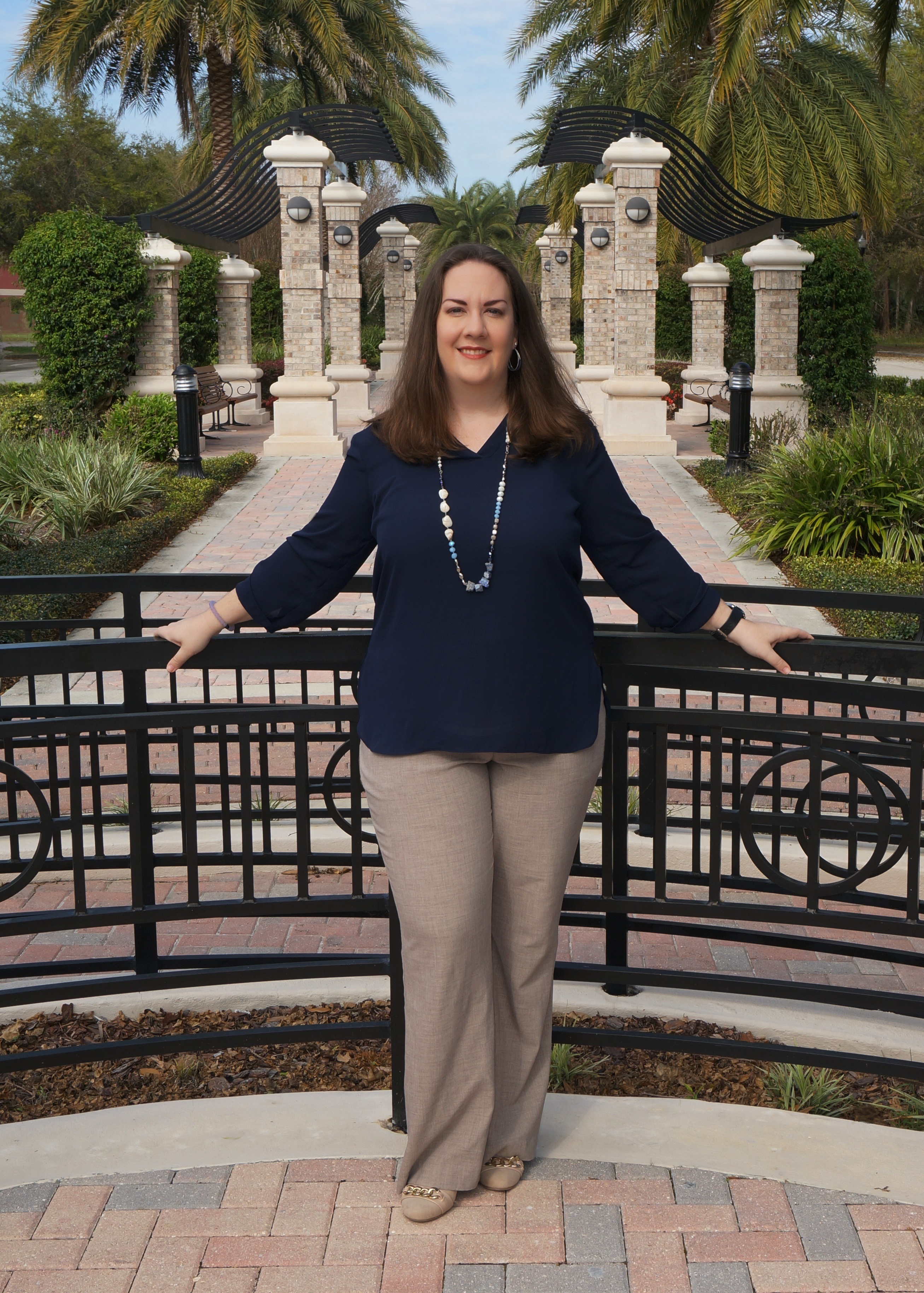 Rebecca Stone standing in front of green hedge wearing a blue blouse and natural stone blue necklace